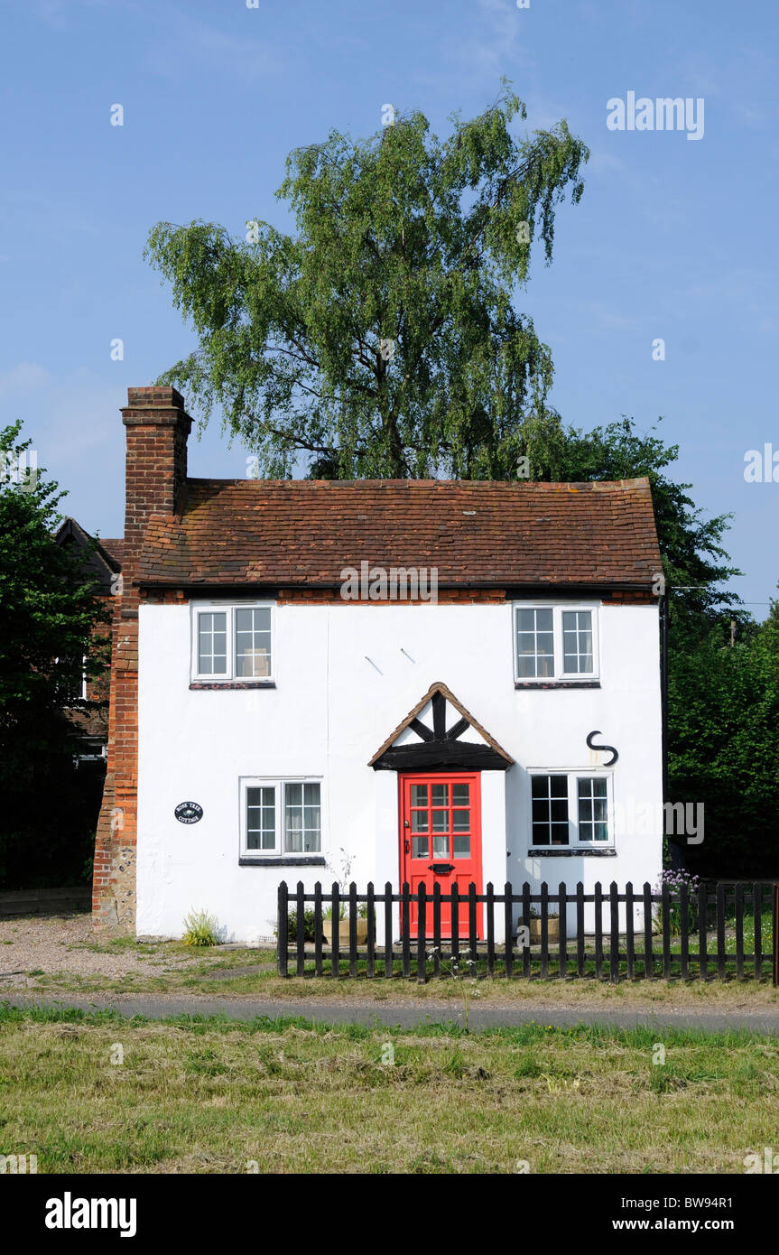 A white tiled english country cottage with red door and garden seen from the front. Stock Photo