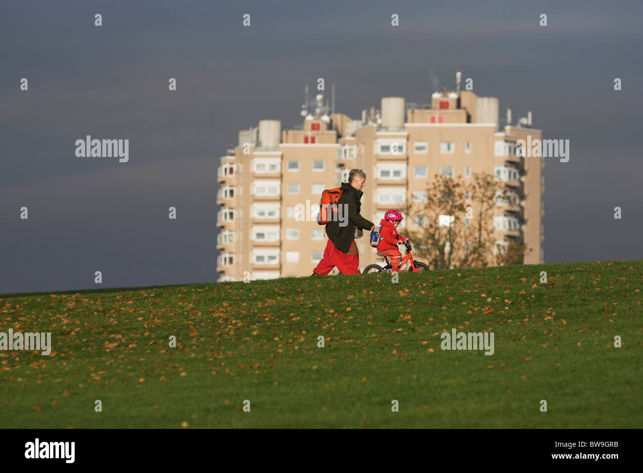 Local mother and child on bike with high-rise flats seen from Brockwell Park, Herne Hill, South London. Stock Photo