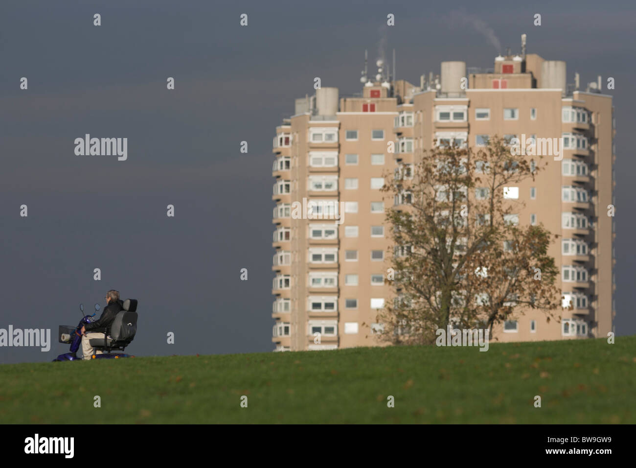 Local disabled man in motorised wheelchair and high-rise flats seen from Brockwell Park, Herne Hill, South London. Stock Photo
