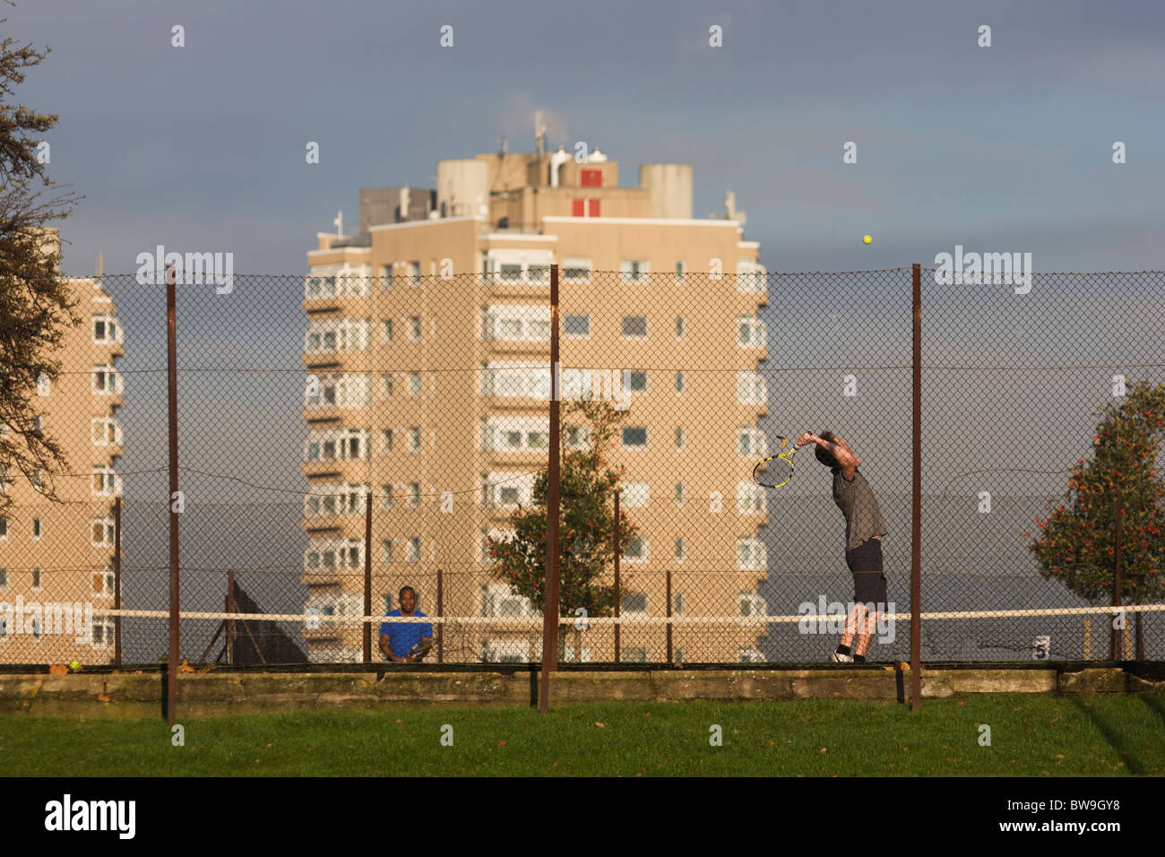 Amateur tennis serve in local court near high-rise flats seen from Brockwell Park, Herne Hill, South London. Stock Photo