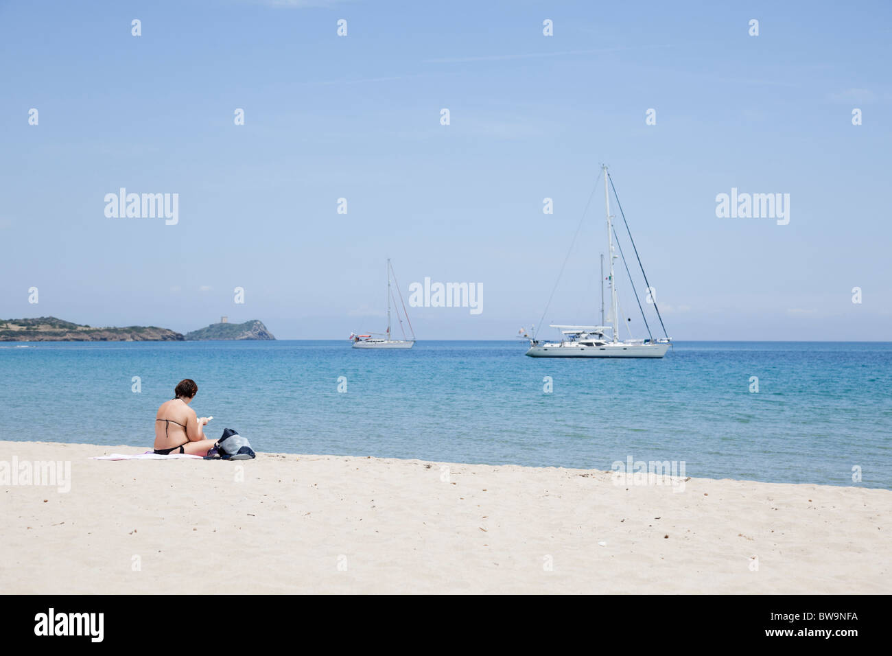 The woman in bikini sitting on sandy beach, relaxing, reading a novel. Stock Photo