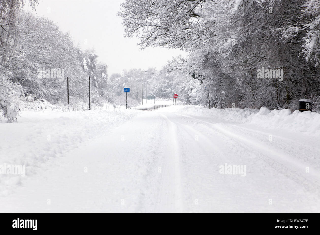 A snow covered road with No Entry and Exit signs in the distance, focus is on the signs. Stock Photo