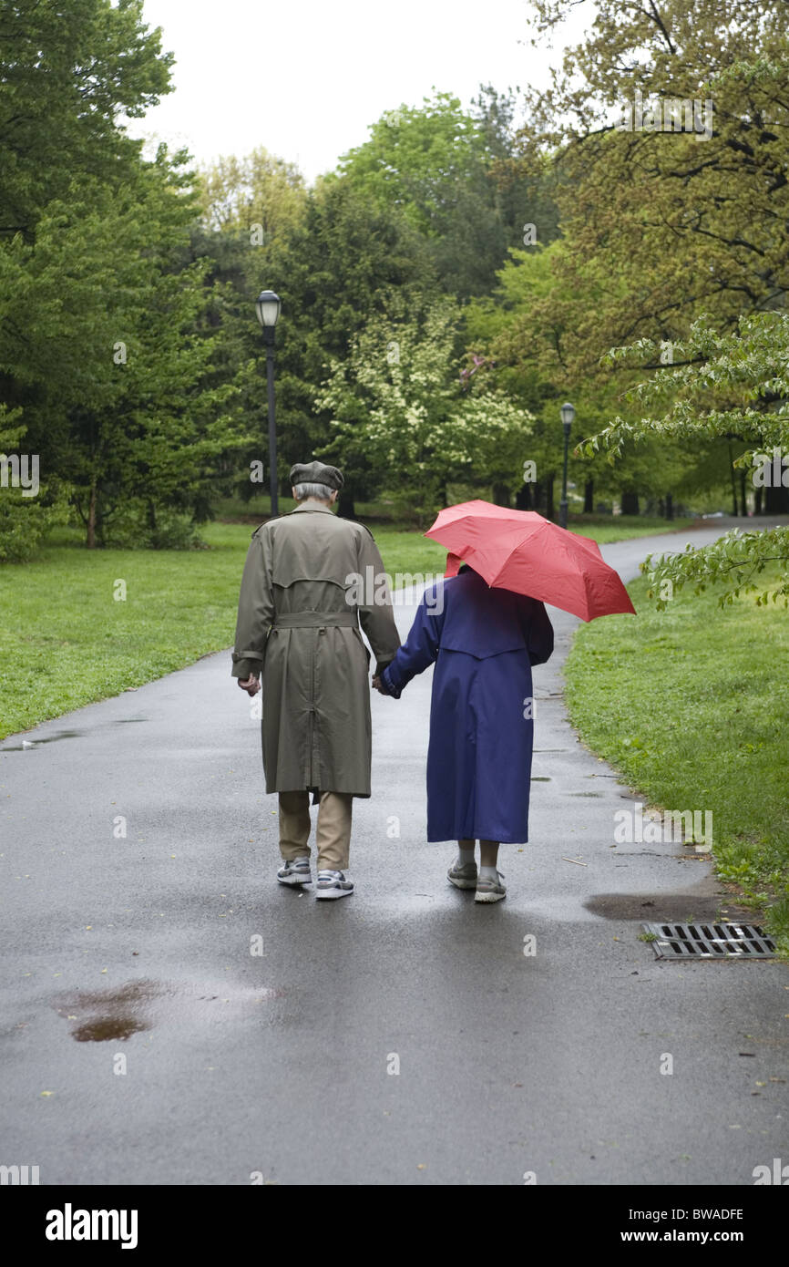 Old couple, hand in hand walk in Prospect Park on a rainy day in Brooklyn, New York. Stock Photo