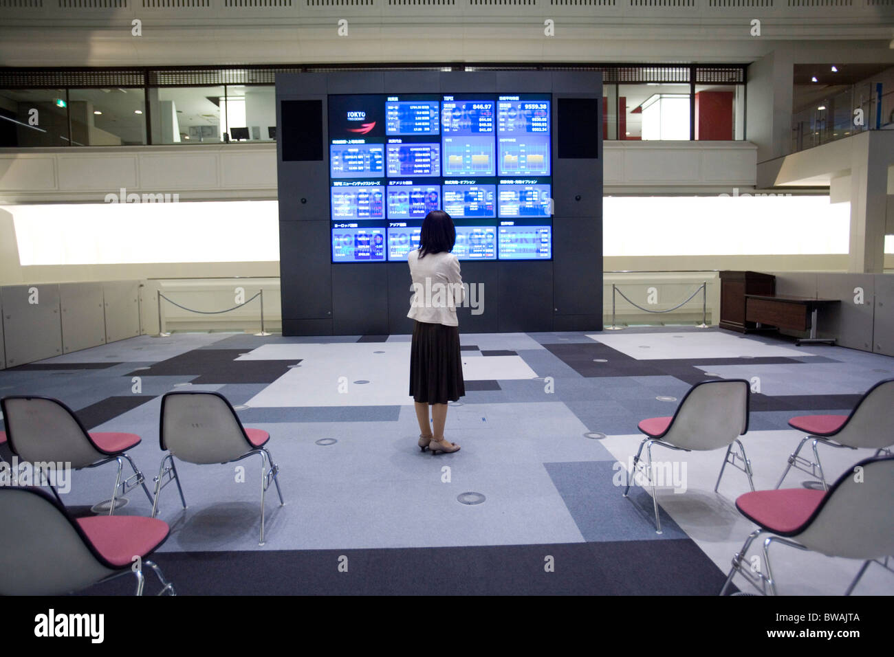 Woman standing in front of monitors at Tokyo stock exchange, Japan. Stock Photo