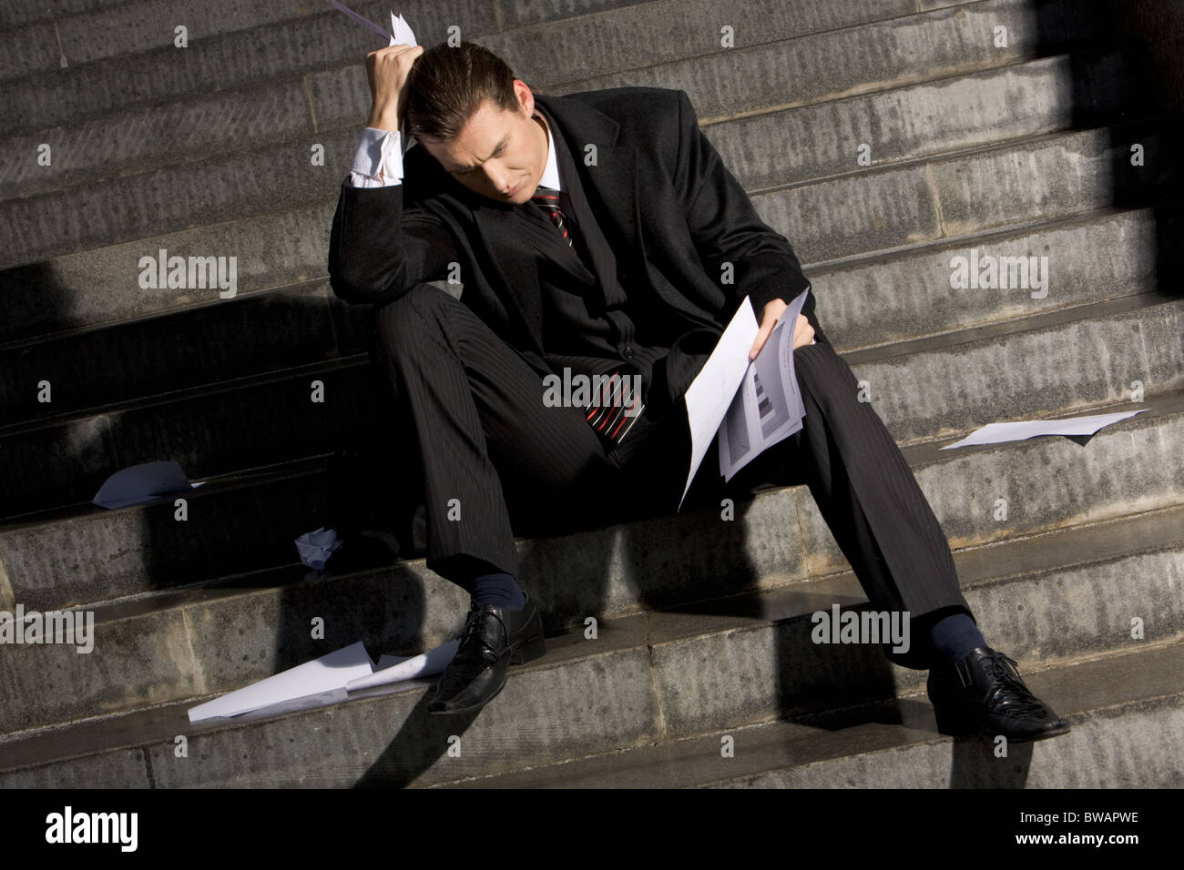 Photo of sad man with papers in hands sitting on stairs with no idea what to do Stock Photo