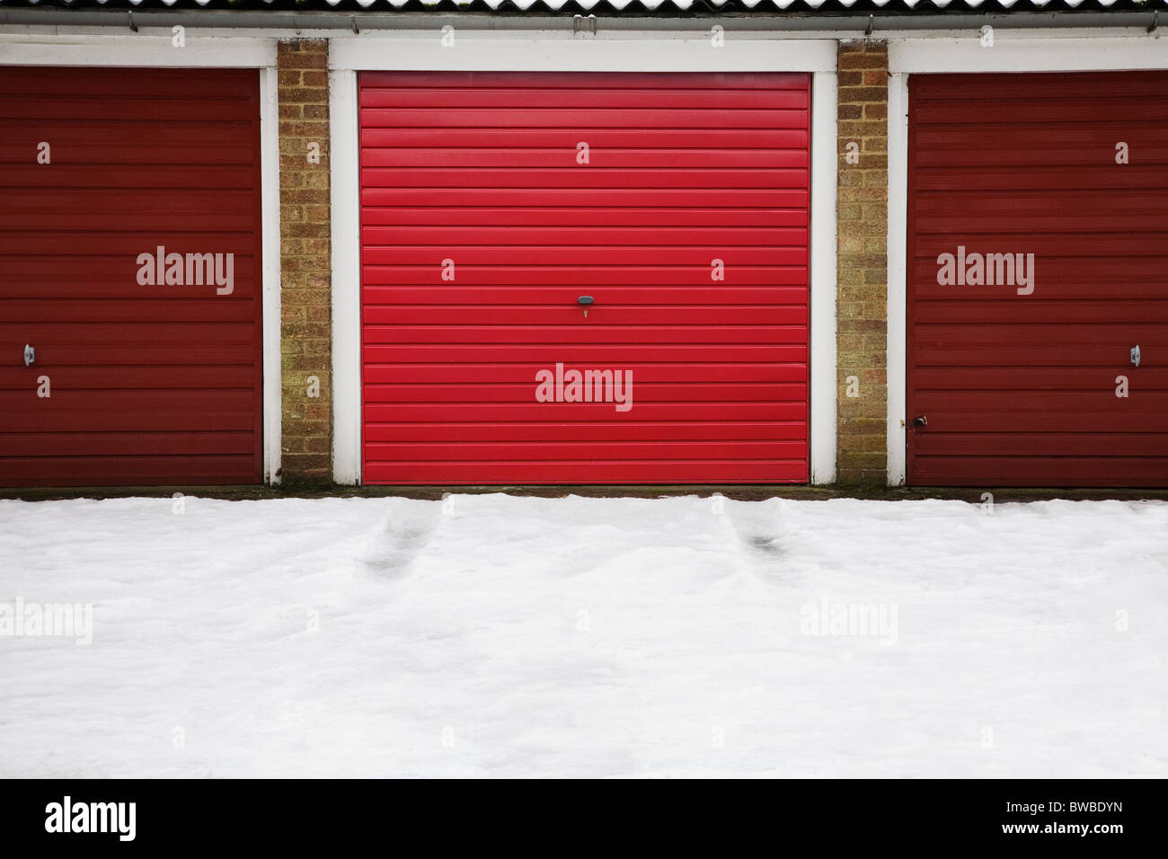 Row of Red garages with vehicle tyre tracks in the snow from centre garage, Stock Photo