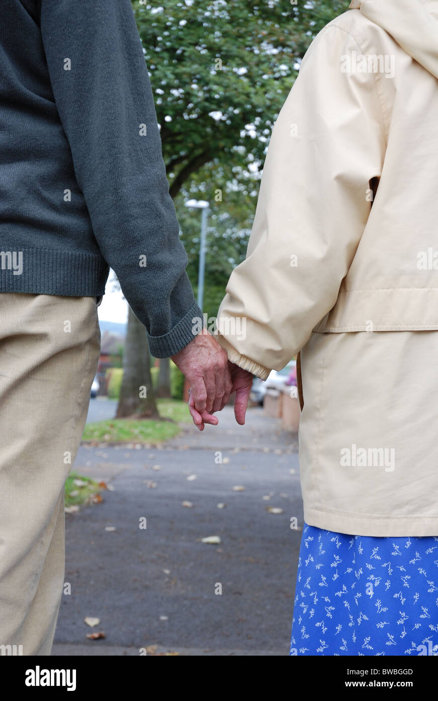 Elderly married couple holding hands walking down a UK street Stock ...
