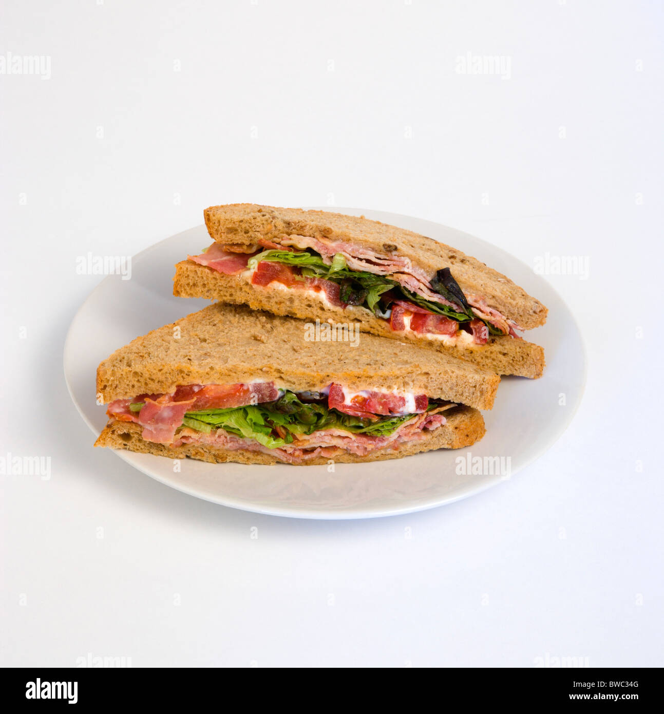 Food, Meal, Snack, Bacon lettuce and tomato BLT brown bread sandwich on a white plate against a white background. Stock Photo