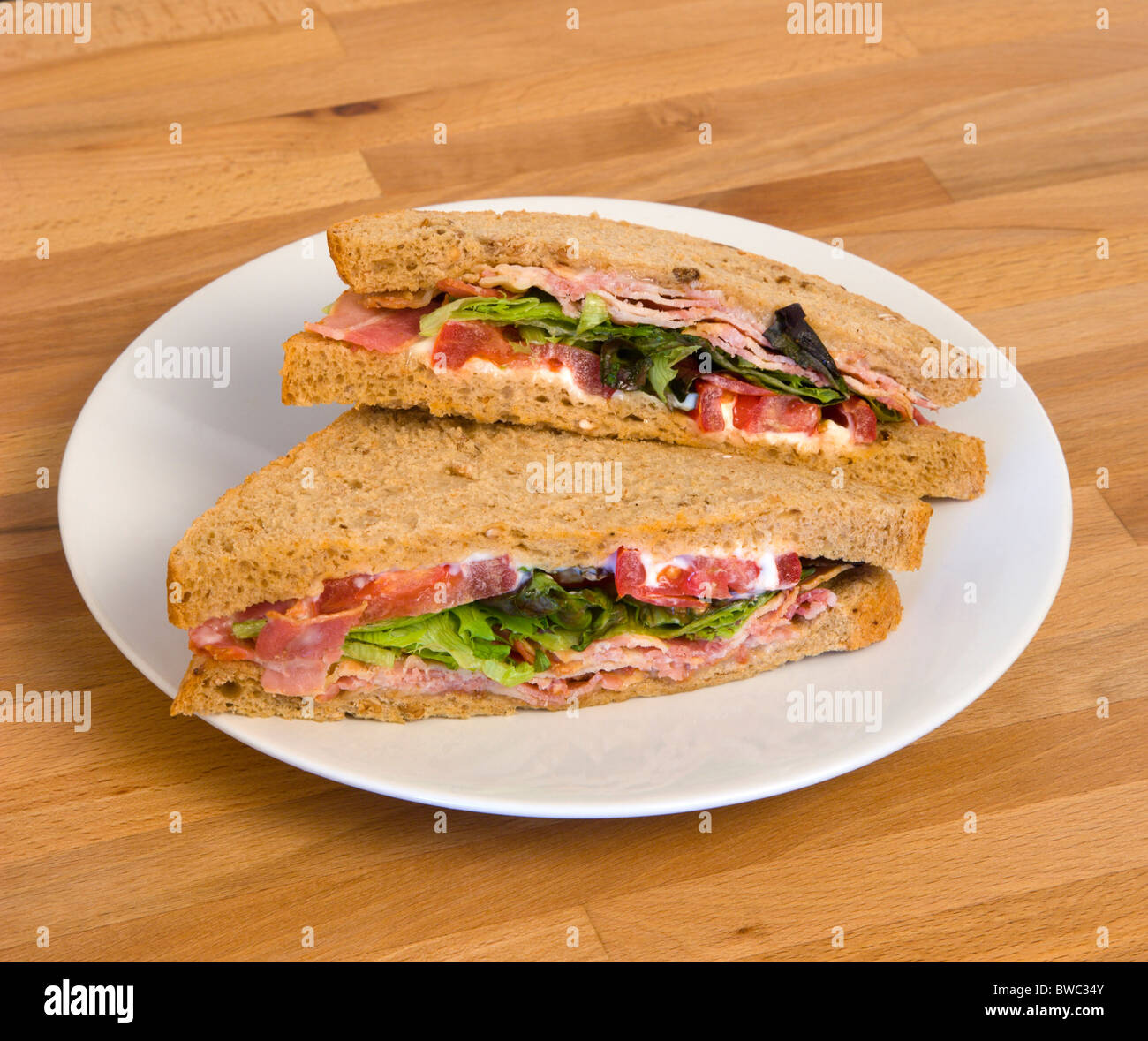 Food, Meal, Snack, Bacon lettuce and tomato BLT brown bread sandwich on a white plate on a wooden table top. Stock Photo