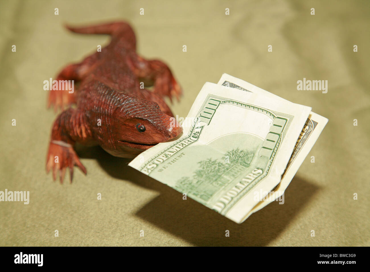 Wooden komodo dragon lizard souvenir carving biting US 100 dollar bill currency bank note in it's mouth Stock Photo