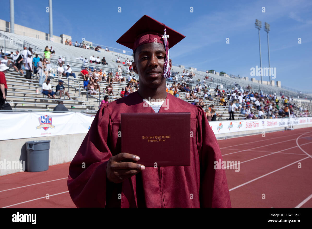 African-American student displays high school diploma at outdoor graduation ceremony taken place during the state track meet Stock Photo
