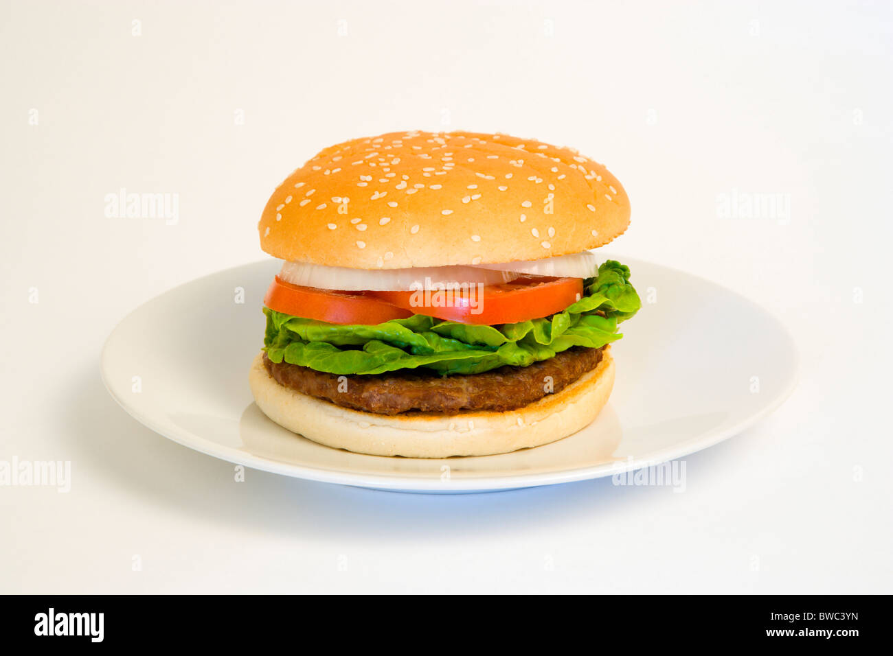Food, Cooked, Hamburger, Single quarter pound burger with onion tomato and lettuce in a bun on a plate on a white background. Stock Photo