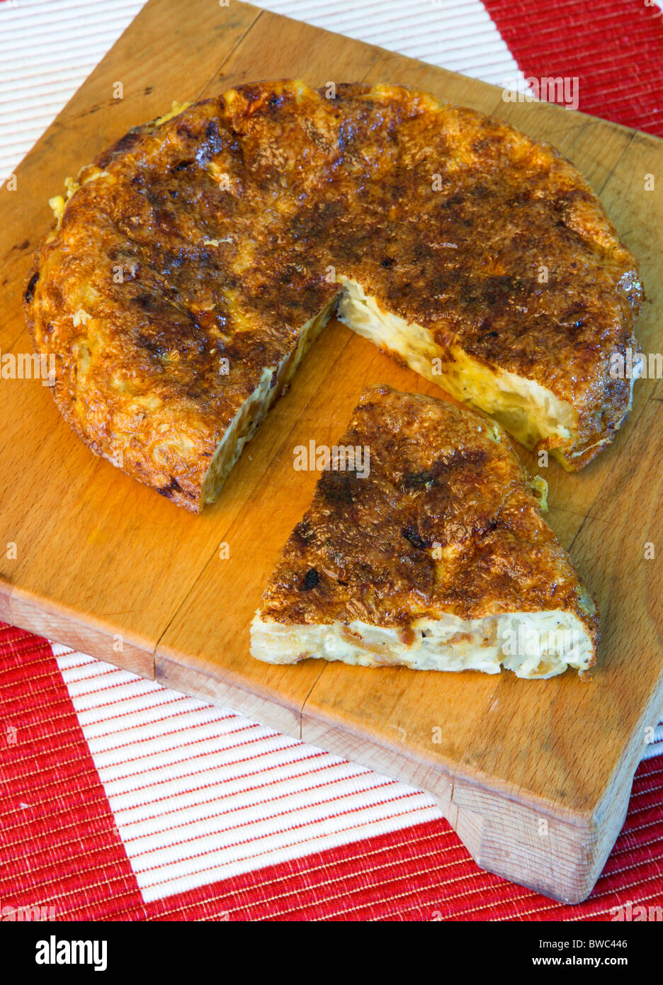 Food, Cooked, Eggs, Spanish omelette or tortilla on a wooden chopping board with a slice cut out. Stock Photo