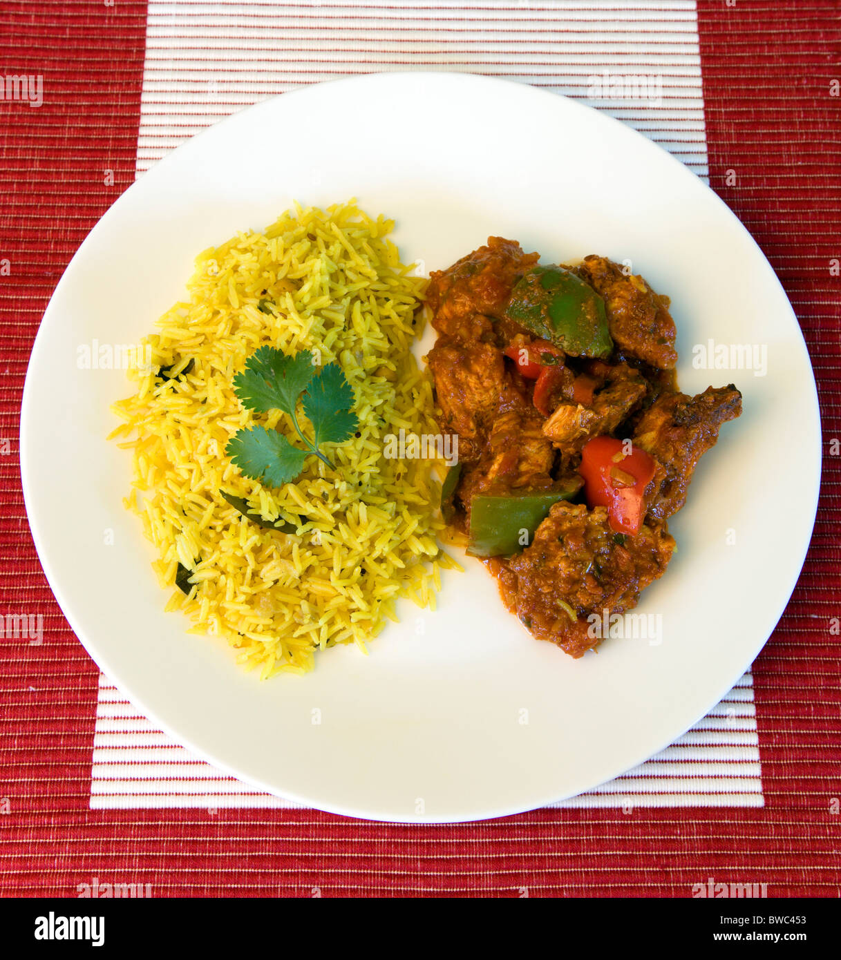Food, Cooked, Curry, Indian chicken Jalfrezi curry with yellow pilau rice on a white plate. Stock Photo