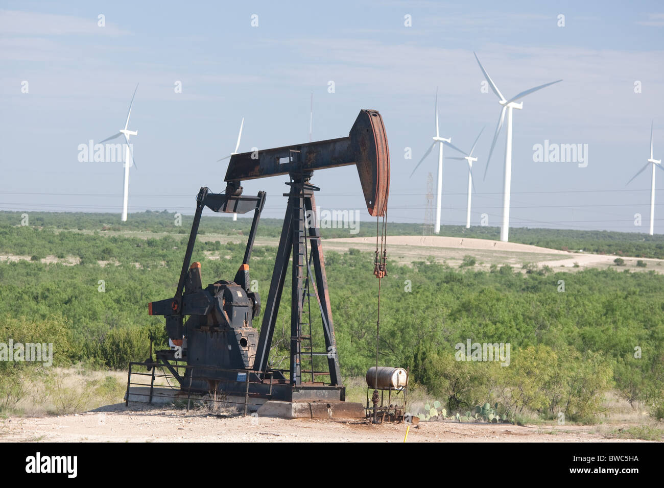 Pumpjack in an oil field adjacent to a wind farm of hightech wind