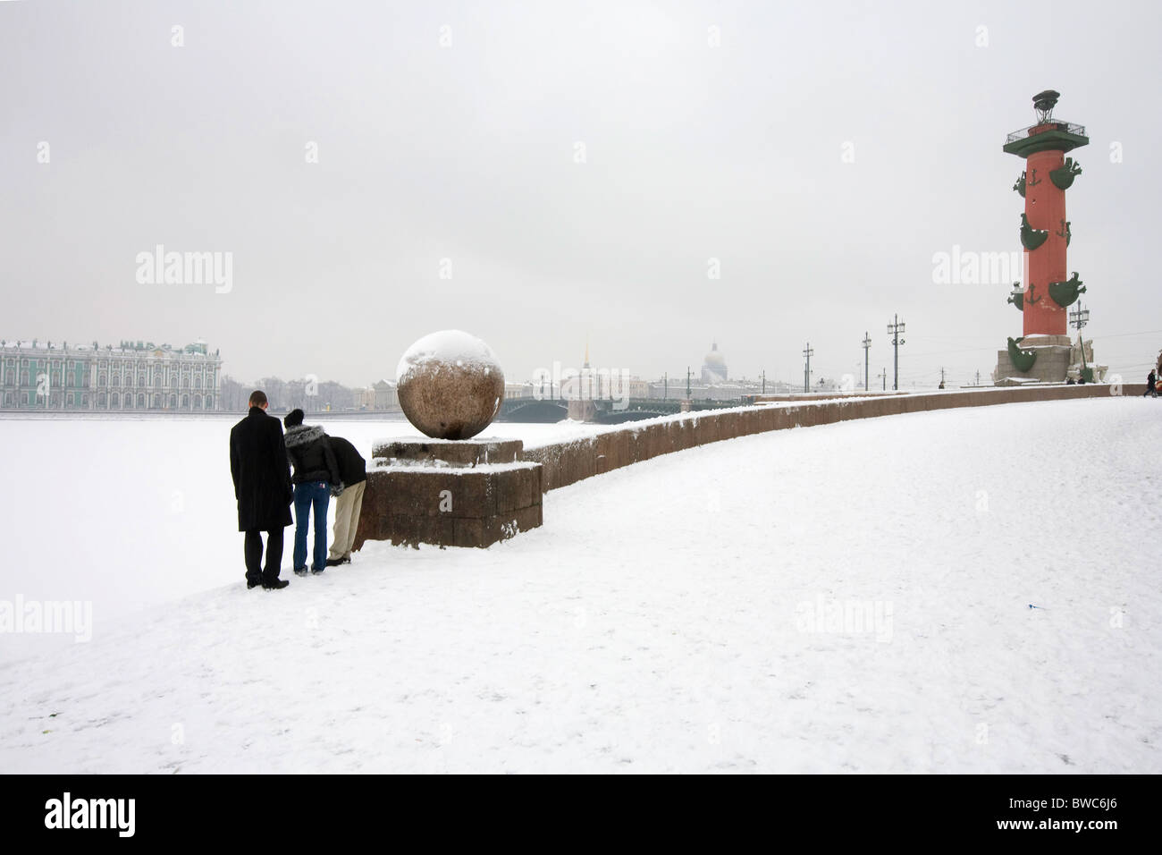 Three young people looking into the snow of the Neva across from 'Winter Palace', St Petersburg Russia Stock Photo