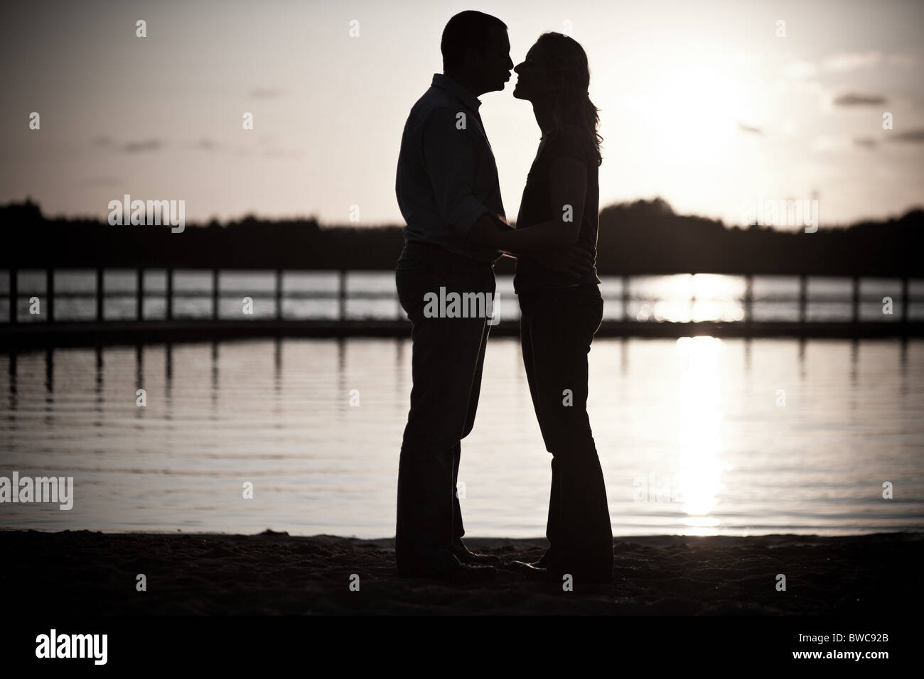 Silhouette of a romantic couple against a sunset in front of the water ...