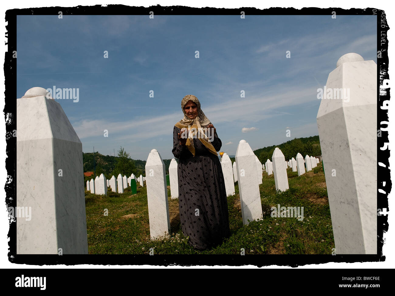 A Bosnian Muslim woman prays between graves of her relatives, all victims of the Srebrenica genocide, at the cemetery in Potocari near Srebrenica, Bosnia and Hercegovina. More than 8,000 Bosnian Muslim men and boys were killed after the Bosnian Serb Army attacked Srebrenica, a designated UN safe area, on 10-11 July 1995, despite the presence of UN peacekeepers. Stock Photo