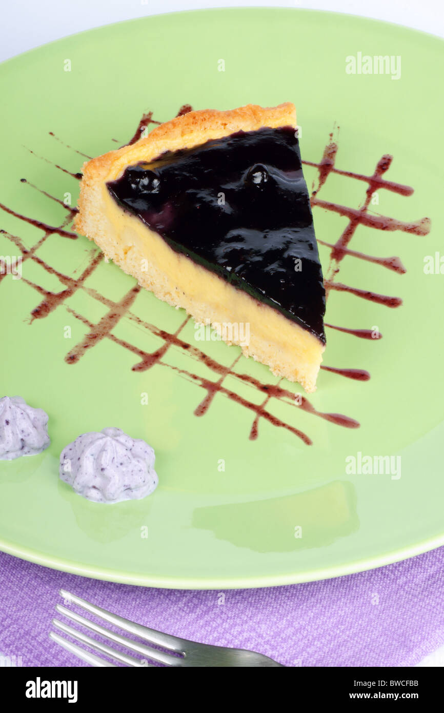 Slice of homemade blueberry marmalade and vanilla custard cream tart over a light green plate. Stock Photo