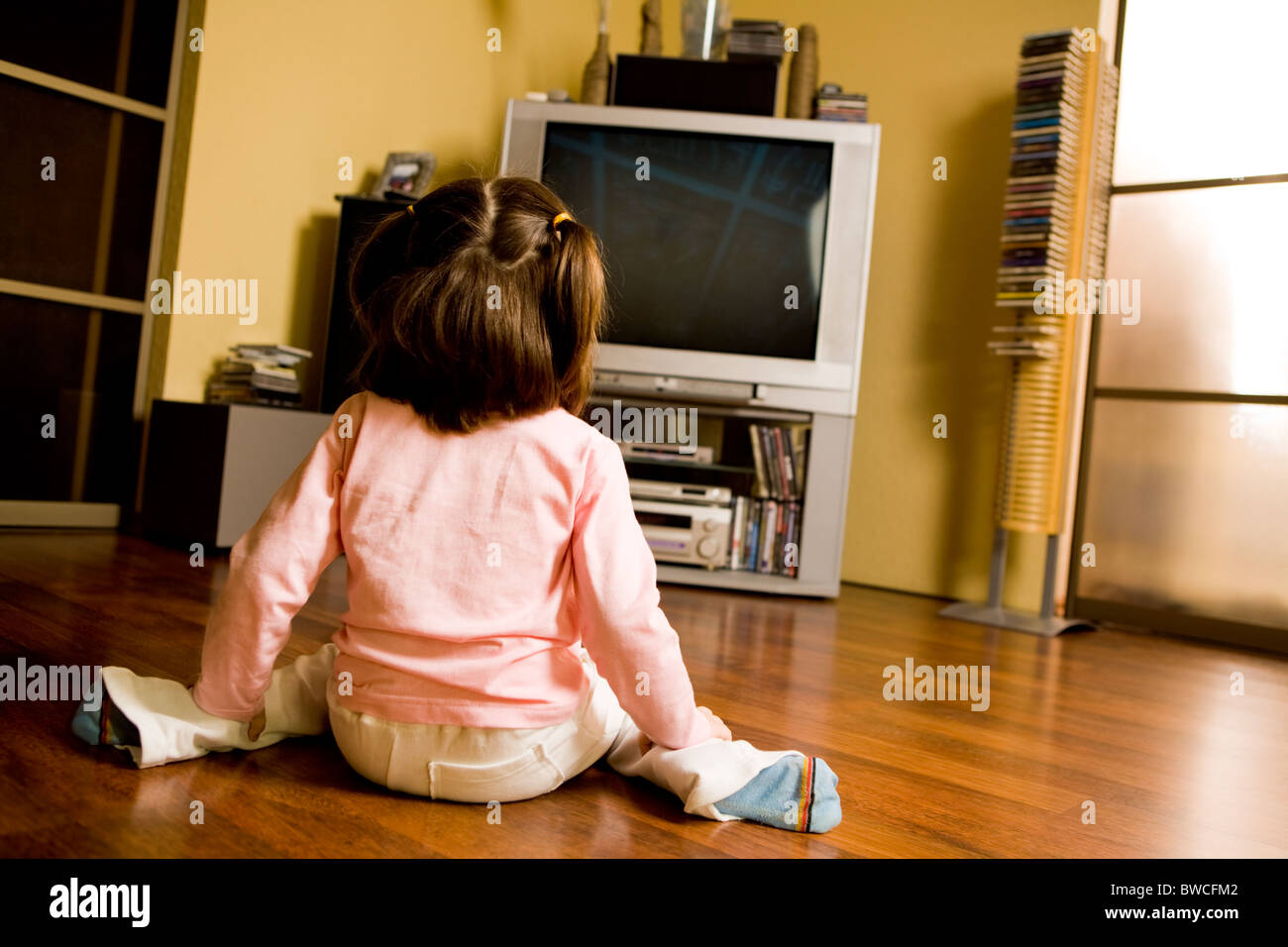 Rear view of little girl sitting on the floor and watching TV in living ...