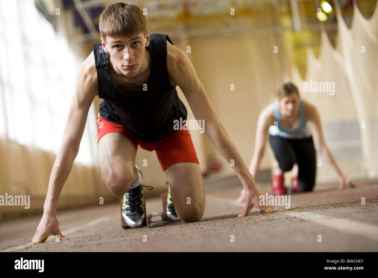 Image of serious young man ready to start running with sportswoman at background Stock Photo