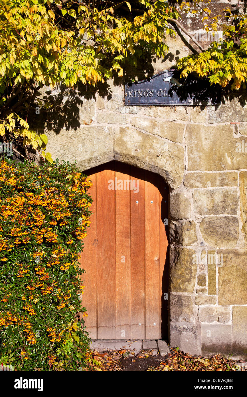 A small old wooden doorway in a stone wall surrounded by orange pyracantha berries Stock Photo