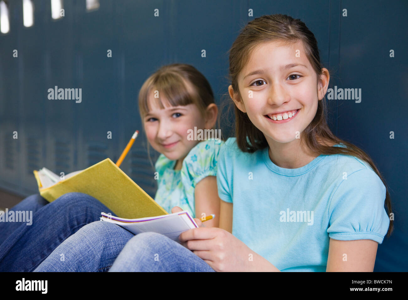 USA, Illinois, Metamora, Portrait of two girls (8-9) sitting at lockers in school corridor and doing homework Stock Photo
