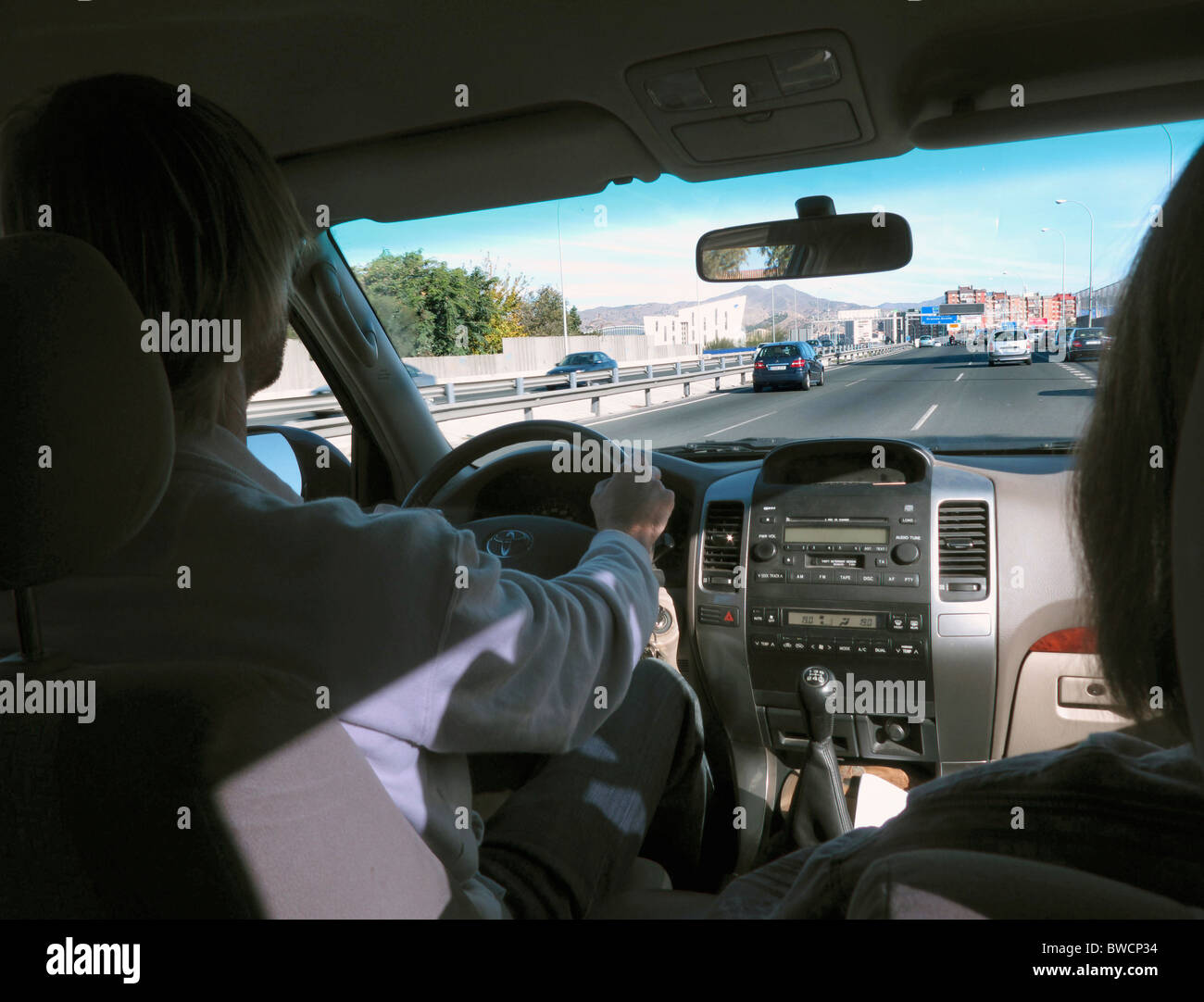Outskirts of Malaga, Spain seen from inside vehicle with driver and passenger. Stock Photo