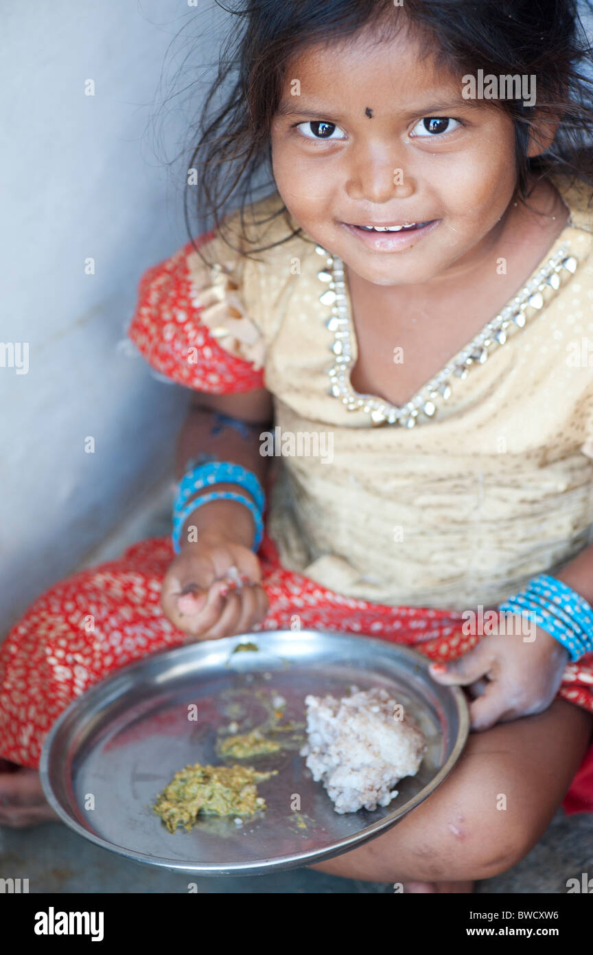 Small Indian rural village girl eats rags ball for breakfast, in the doorway of her home. Andhra Pradesh, India Stock Photo