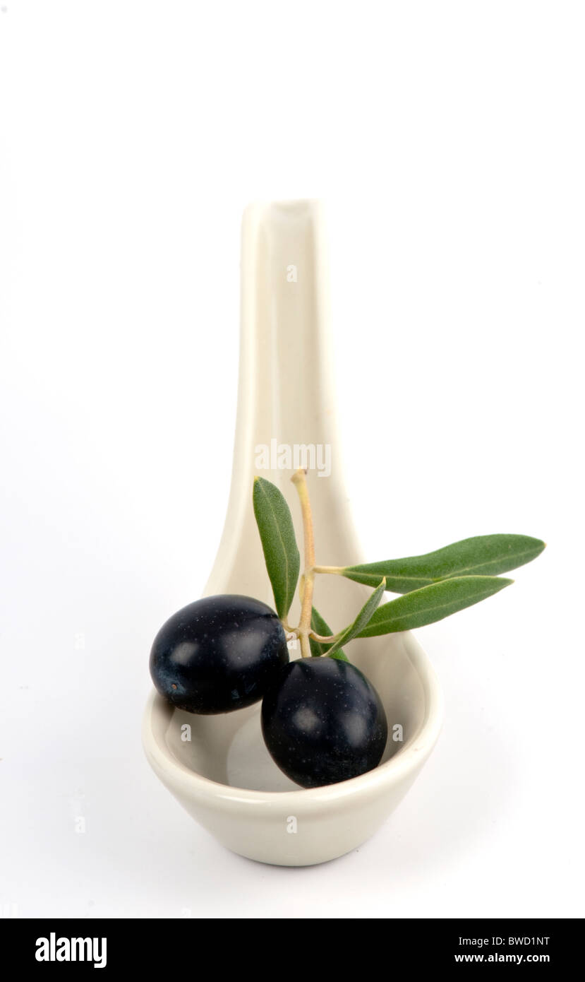 Two freshly picked black olives with a few leaves in a ceramic spoon. On white. Stock Photo