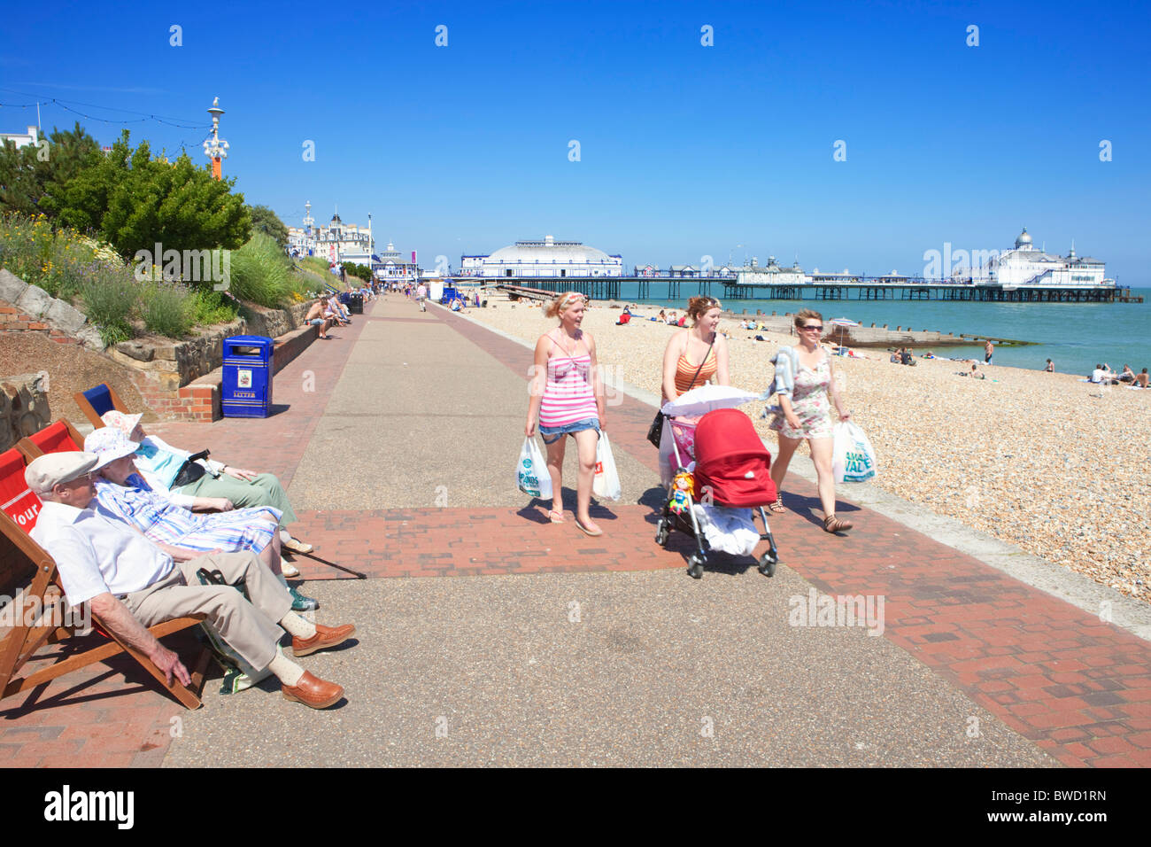 Old people on deck chairs watching young people walk along promenade; Eastbourne; East Sussex; England, Great Britain Stock Photo