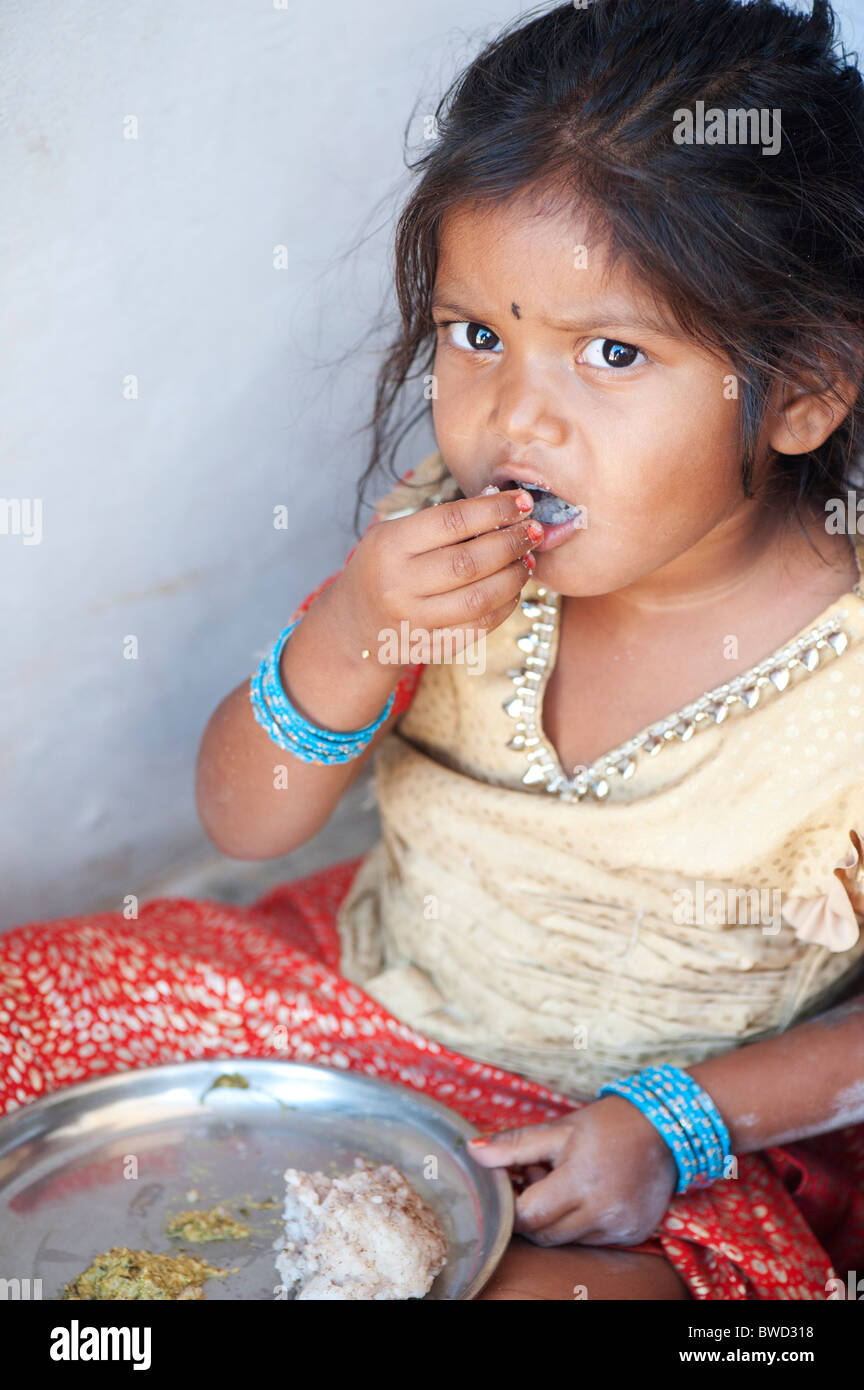 Small Indian rural village girl eats rags ball for breakfast, in the doorway of her home. Andhra Pradesh, India Stock Photo