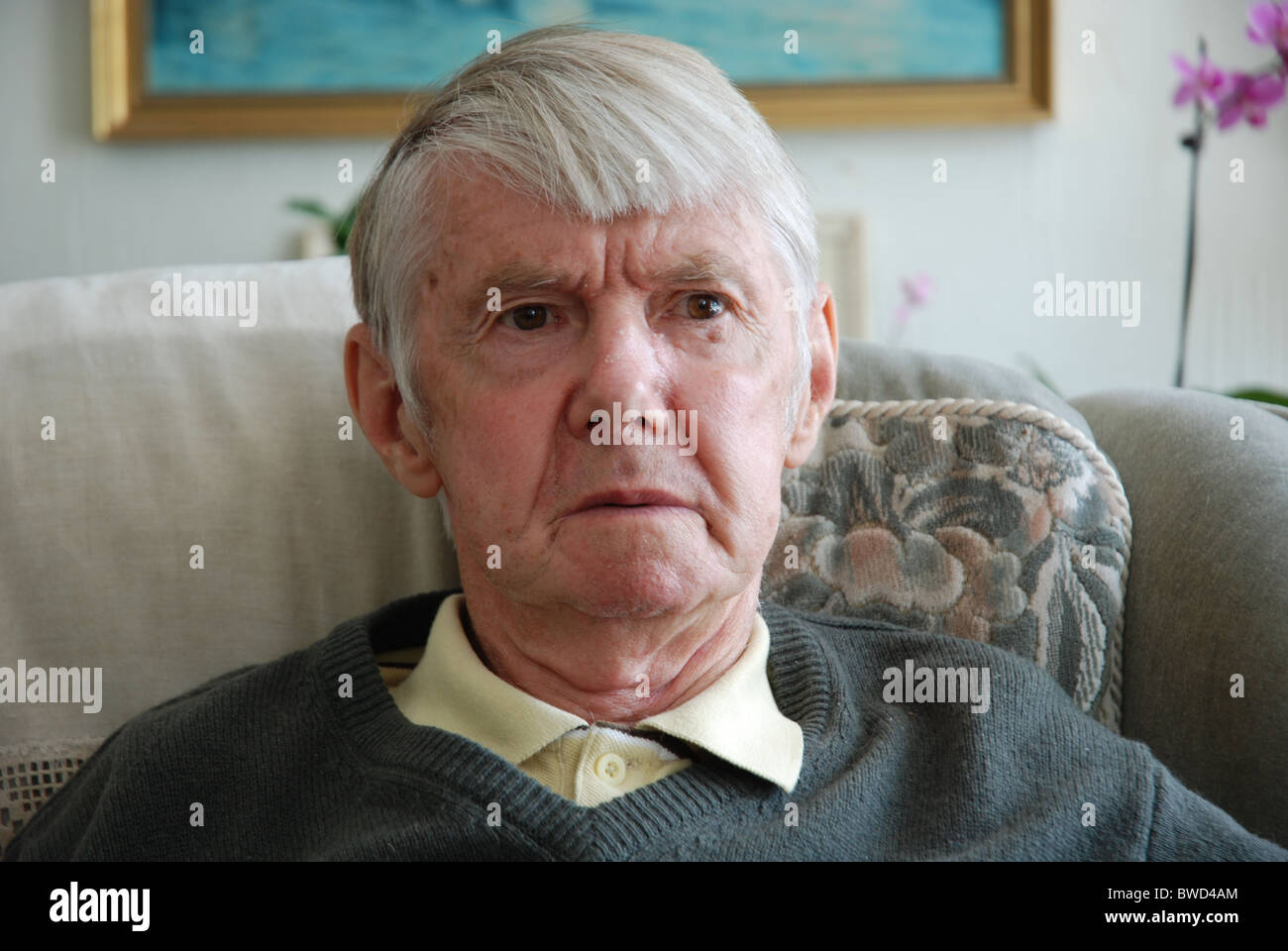 Old man sitting in a chair in his home staring outwards Stock Photo