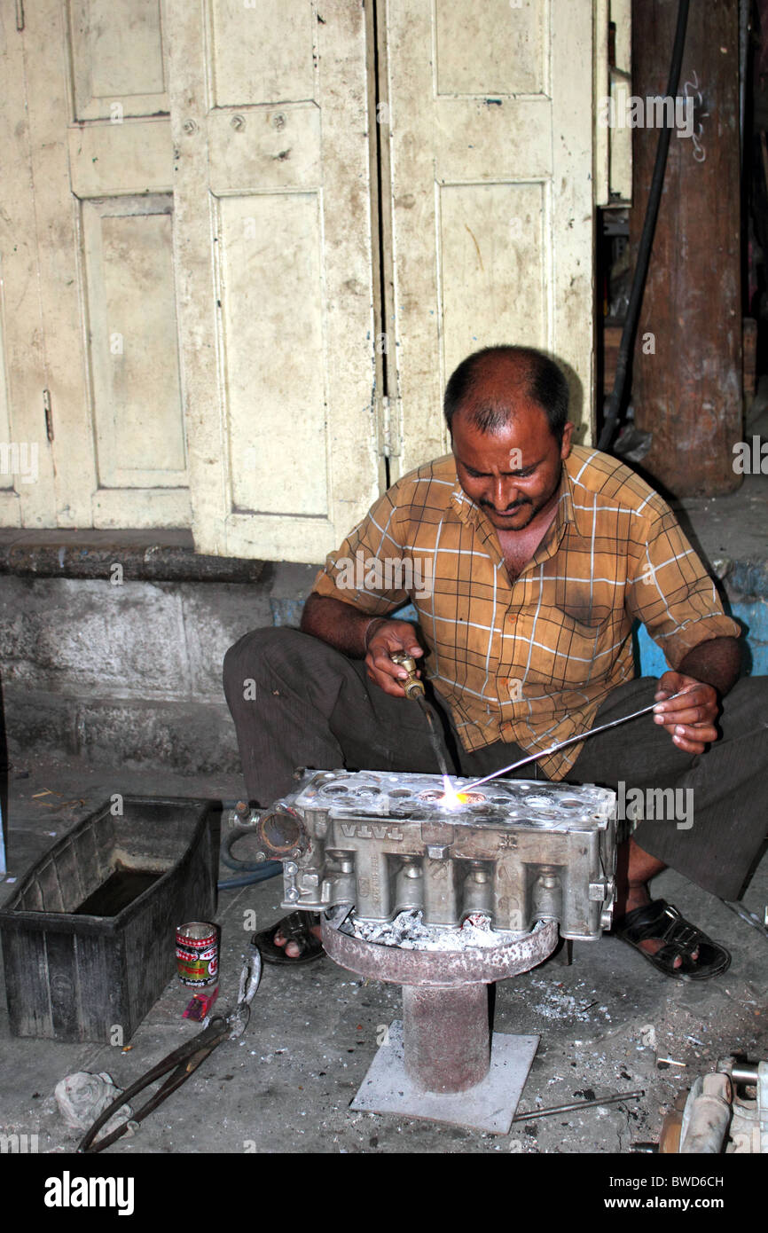 Indian man repairing car engine block by welding cylinder head using a gas torch but not wearing
