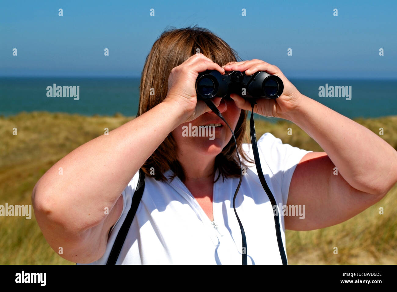 Lady looking through binoculars on the beach at Winterton on Sea, Norfolk Stock Photo