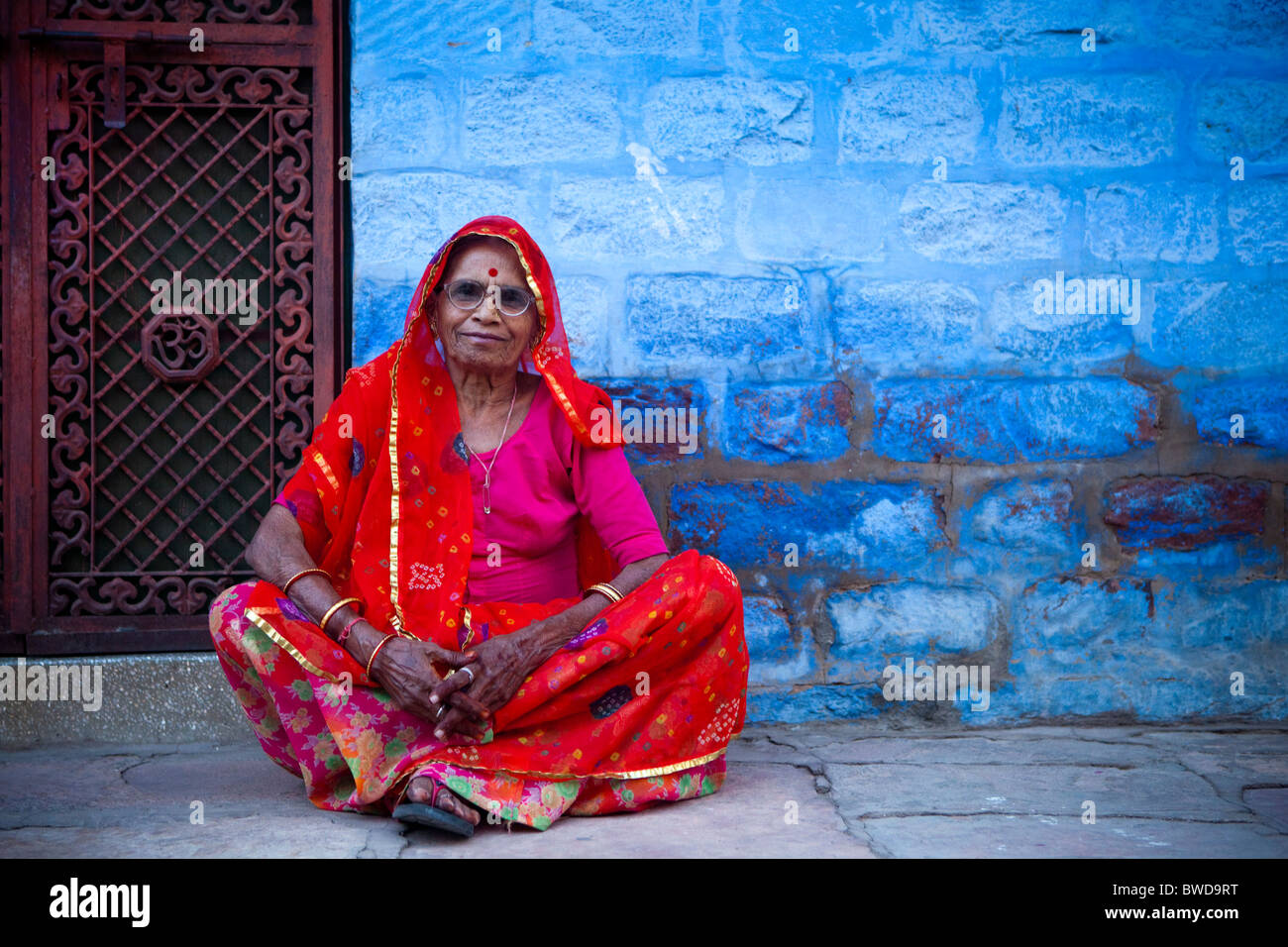 Old lady in red sari against the traditional Blue Architecture of Jodhpur. Stock Photo