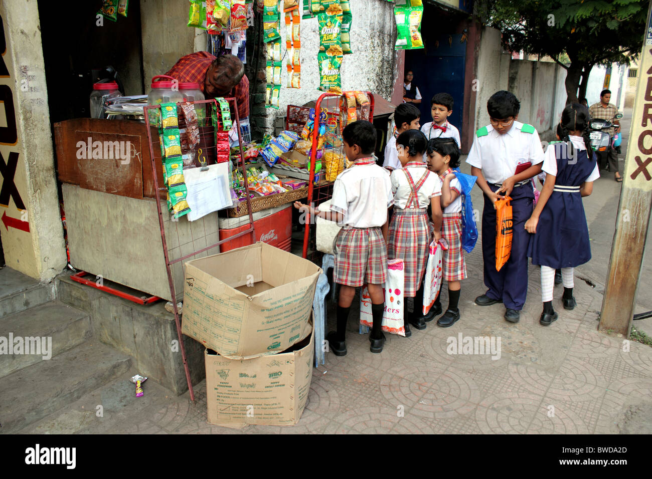 Indian school children in uniform gather around a small shop on the street to buy treats before going to school; Hyderabad India Stock Photo