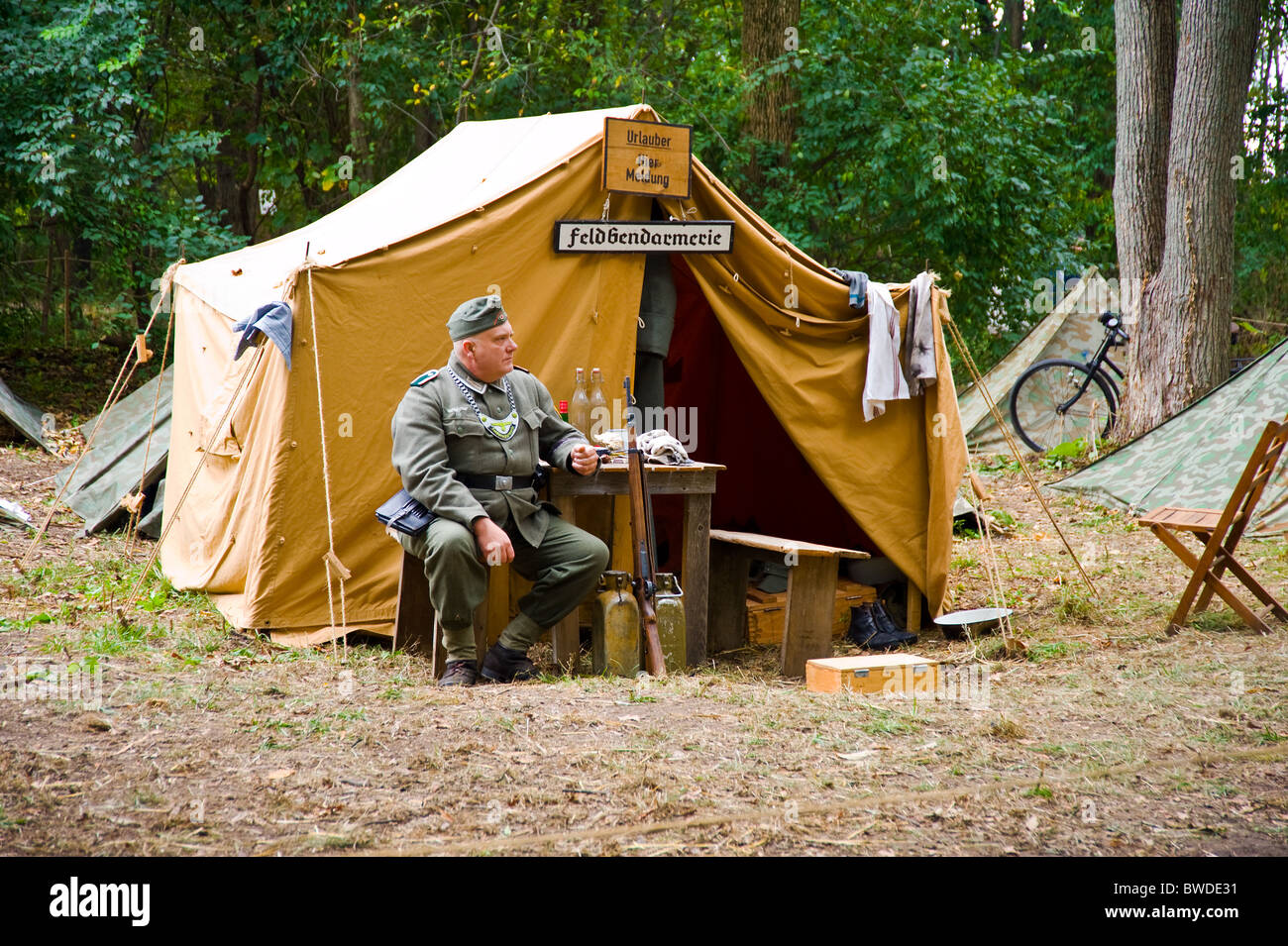 German army officer world war two time sitting near tent camp camping acting show wood forest bench table Stock Photo