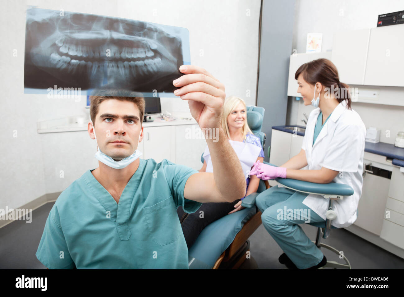 Radiodentist checking x-ray with assistant and patient having conversation in the background Stock Photo