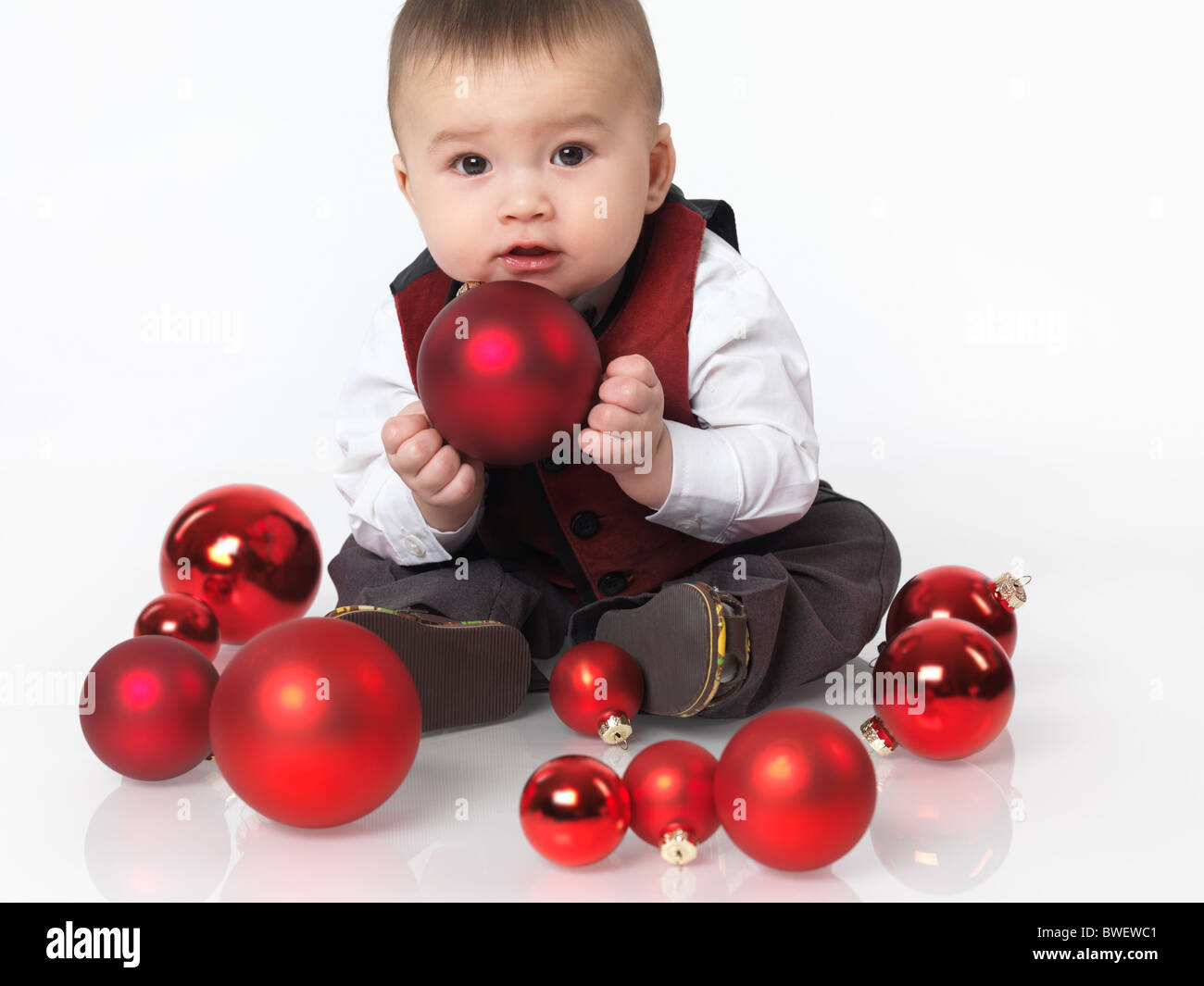 Six month old baby boy sitting with a red bauble Christmas decoration in his hands. Isolated on white background. Stock Photo
