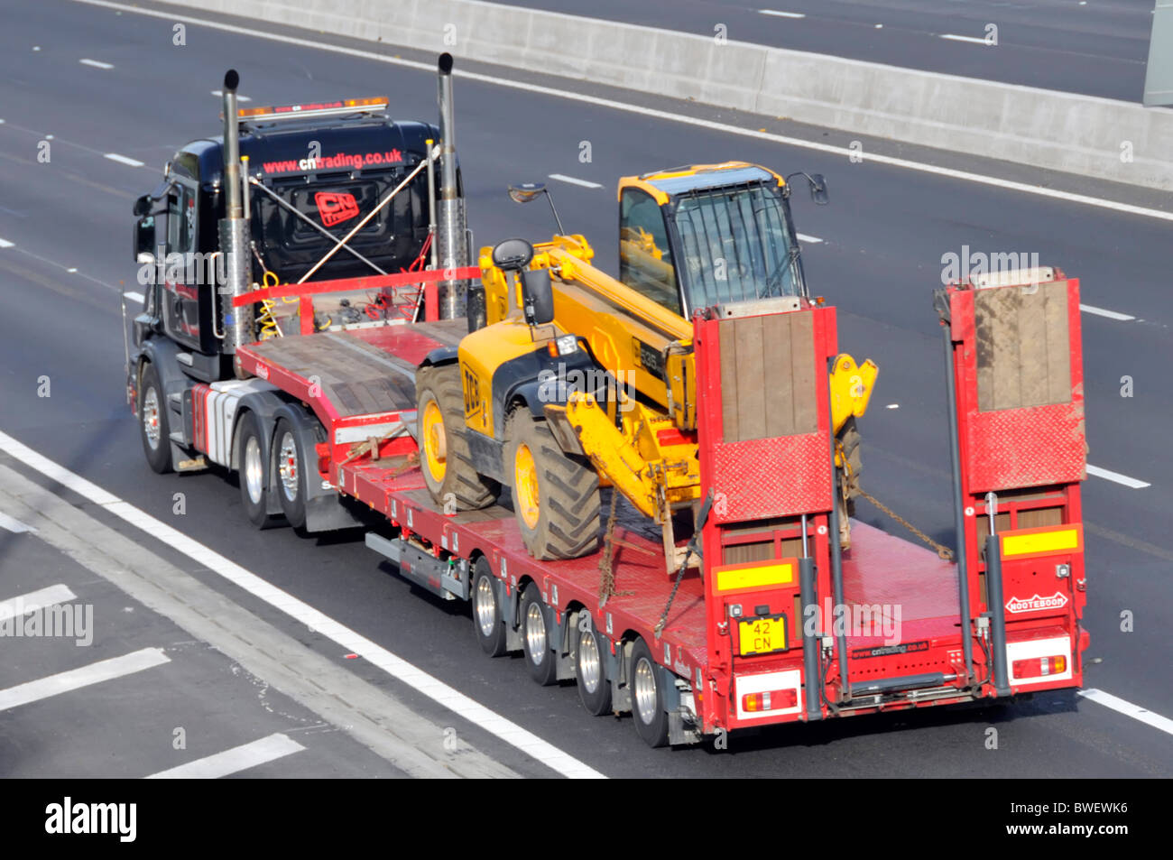 HGV lorry truck & low loader transport for JCB Bamford business diesel hydraulic construction equipment machine driving on motorway England UK Stock Photo