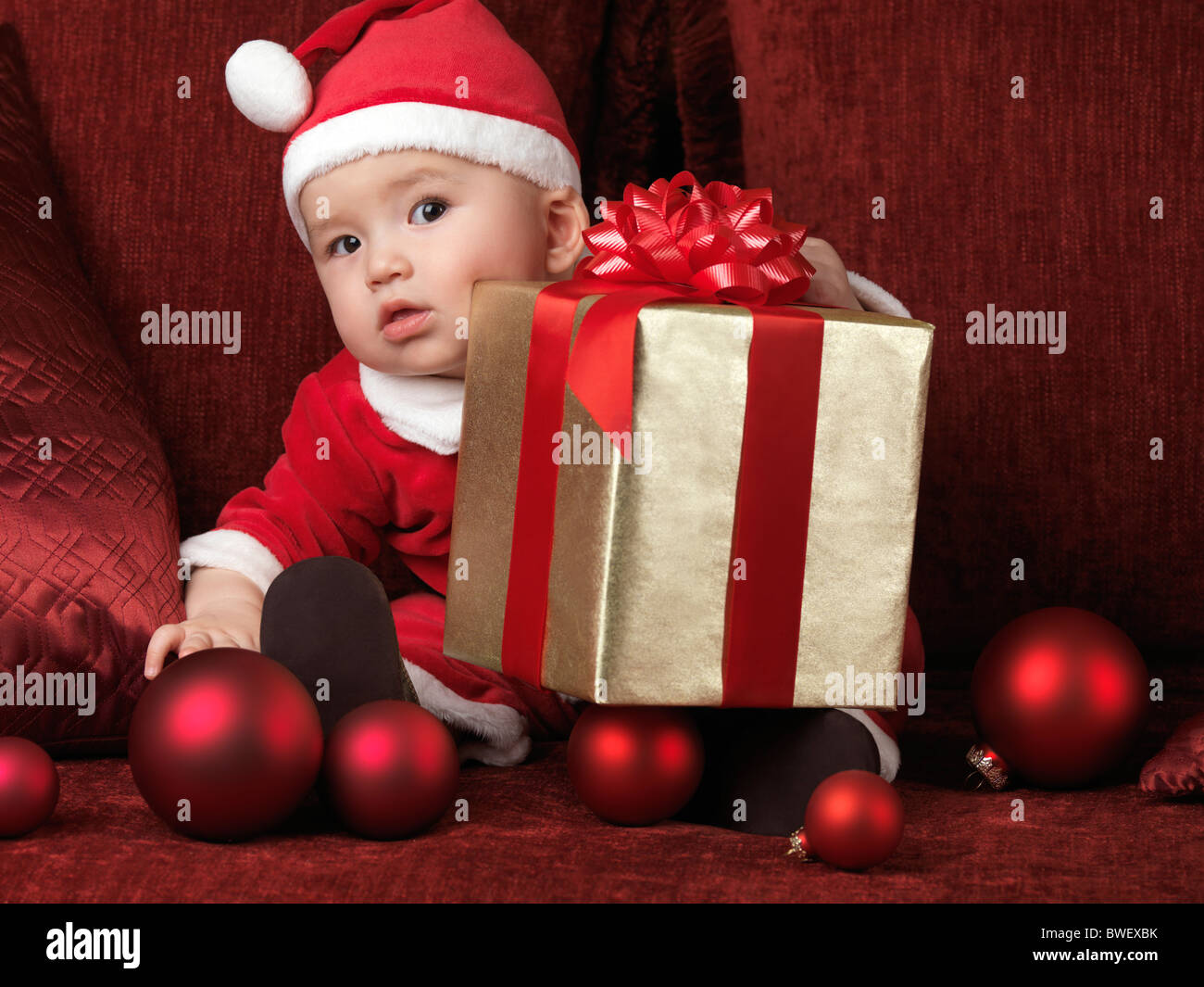 Six month old baby boy in Santa costume with a Christmas present on his lap Stock Photo