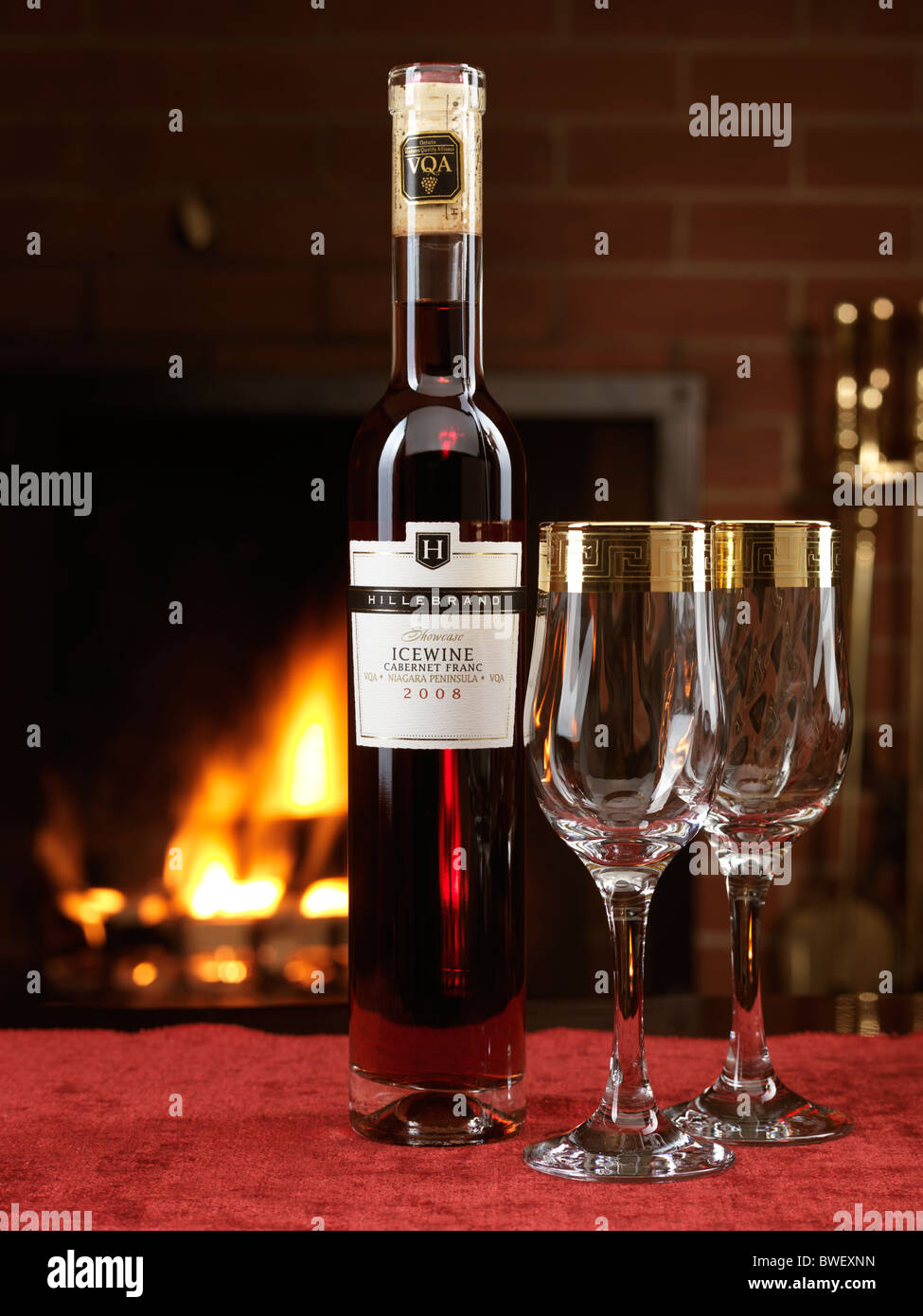 Bottle of red Icewine Cabernet Franc by Hillebrand and two wine glasses on a table with a fireplace in the background Stock Photo