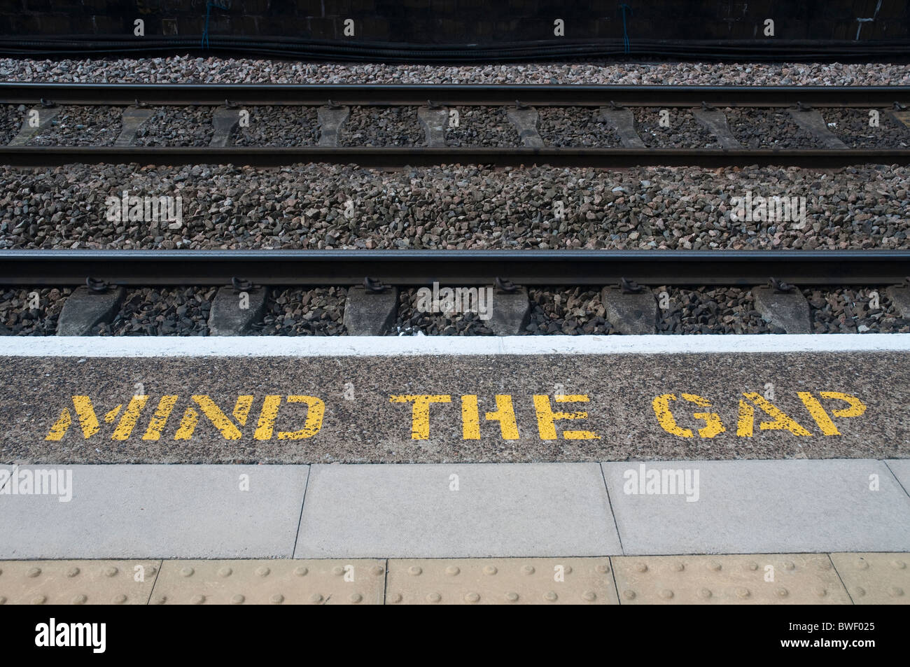 "Mind The Gap" stenciled lettering in yellow on the edge of a railway