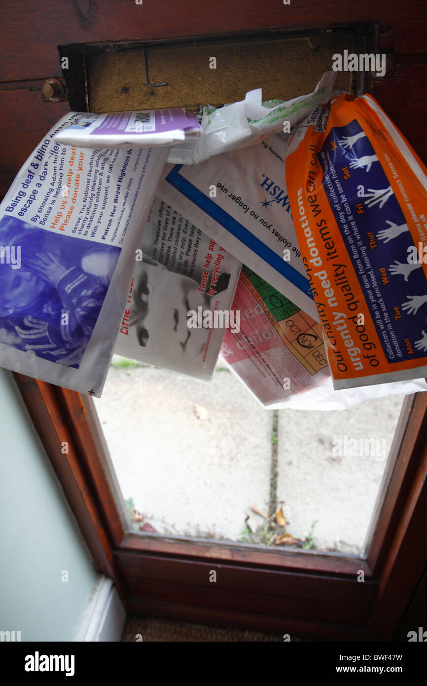 An assortment of charity collection bags stuffed through a letterbox. Stock Photo