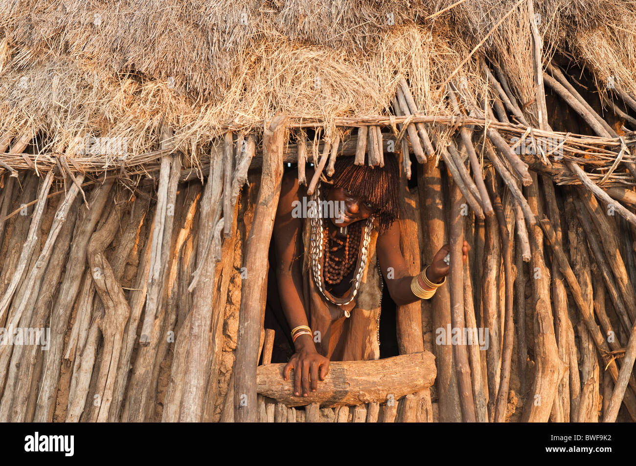 Pregnant Hamar woman with necklaces made of Cowry shells coming out of her wooden hut, Omo river valley Ethiopia Stock Photo
