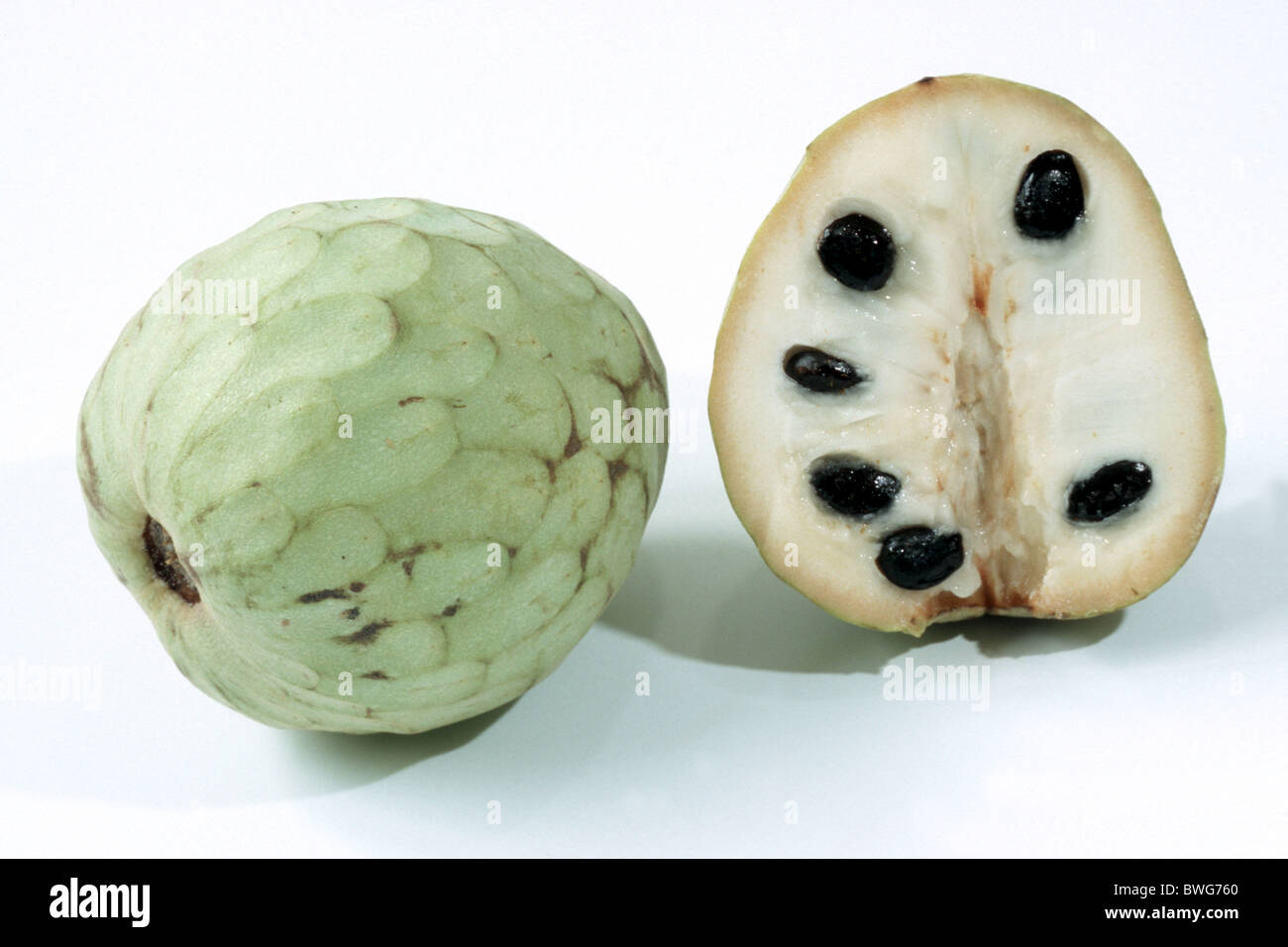 Cherimoya (Annona cherimola), one whole and one halved fruit, studio picture. Stock Photo