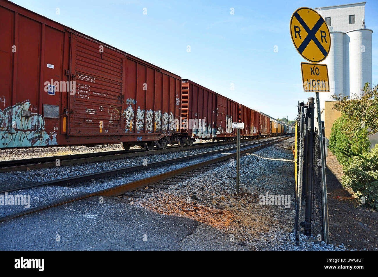 Railroad crossing showing sign and train on tracks. Stock Photo
