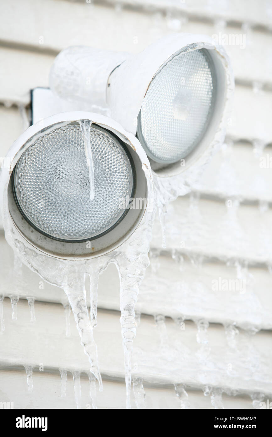 ice and icicles form on light fixture on siding of a house Stock Photo