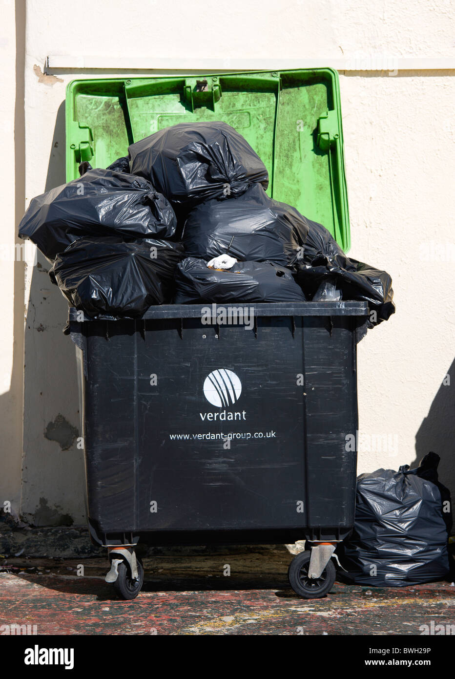 England, West Sussex, Bognor Regis, Wheeled waste bin container overflowing with full large black refuse sacks and bags. Stock Photo